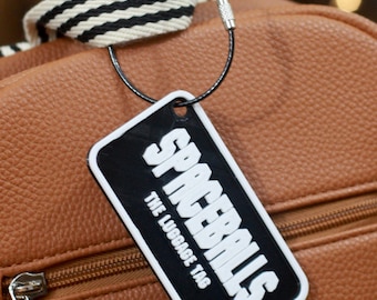 May include: A brown leather luggage tag with a black and white logo that says "Spaceballs The Luggage Tag".
