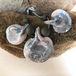 May include: A necklace featuring three ceramic pendants in shades of pink and blue with a marbled effect. The pendants are strung on a cord with dark grey beads.