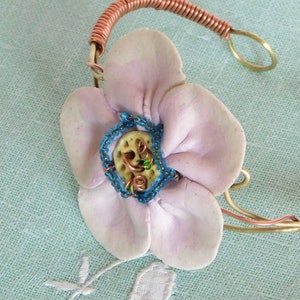 Könnte beinhalten: Ein zartes rosa Blütenblatt mit einem blauen Perlenkern ist an einem Kupfer- und Messingdrahtarmband befestigt. Das Armband ist ein einzigartiges und handgemachtes Schmuckstück.