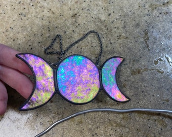 May include: A triple moon pendant made of stained glass with iridescent colors. The pendant is hanging from a silver chain.
