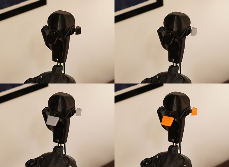 May include: A black, articulated robot head with a rounded top and various attachments. The attachments are shown in black, gray, and orange. The robot head is mounted on a black stand, with a white wall in the background.