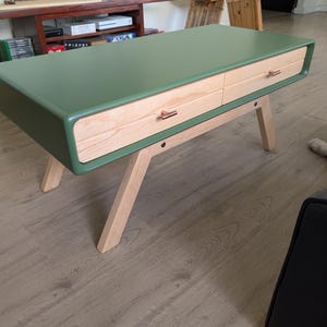 May include: A modern coffee table with a green top and two wooden drawers. The table has light wood legs and copper-colored drawer pulls. The table's dimensions are approximately 48 inches long, 24 inches wide, and 16 inches high.