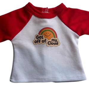 Puede incluir: Una camiseta raglán blanca y roja con el texto "Get off of my Cloud" y un arcoíris sonriente. La camiseta tiene mangas rojas y un cuello rojo. El gráfico está en el centro de la camiseta.