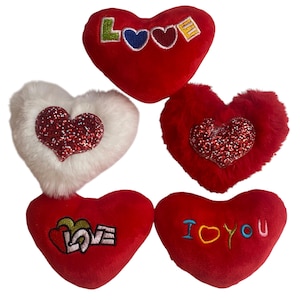 Pode incluir: Cinco almofadas de pelúcia em forma de coração com diferentes desenhos bordados. As almofadas são vermelhas com acabamento de pele branca e apresentam as palavras "Love", "I Love You" e "Love" em diferentes fontes e cores.