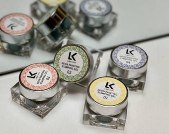 May include: A collection of neon painting stamping gels in small, silver containers with clear acrylic bases. Each gel has a different colored label with the text "LISA KON NEON PAINTING STAMPING GEL" and a number. The colors include pink, green, yellow, and blue.