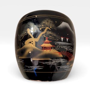 May include: Black, oval-shaped decorative container with a Japanese landscape design. The artwork features a gold tree, a red pagoda, and a bridge. The container has a glossy finish and is likely made of ceramic or lacquer.