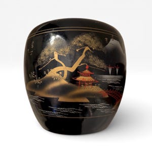 May include: Black, oval-shaped decorative container with a Japanese landscape design. The container features a gold tree, a red pagoda, and a bridge. The background includes mountains and water, all set against a black background.