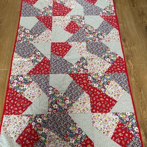 May include: A red, white and blue patchwork quilt with a floral pattern. The quilt is made of squares and triangles and has a red border.