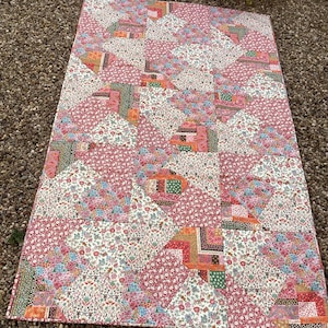 May include: A patchwork quilt with a floral design. The quilt is made up of various fabric pieces in shades of pink, white, orange, and green. The quilt has a rectangular shape and is likely made from cotton.