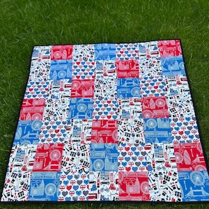 May include: A patchwork quilt featuring a London theme. The quilt is made up of squares of fabric with various designs, including the London Eye, Big Ben, double-decker buses, and the Union Jack flag. The quilt is blue, red, and white.
