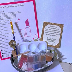 May include: A DIY makeup kit with a guide, palette, brushes, and various cosmetic ingredients. The kit includes a pink and white guide with text, a white palette with three wells, and a small container of orange-colored product.
