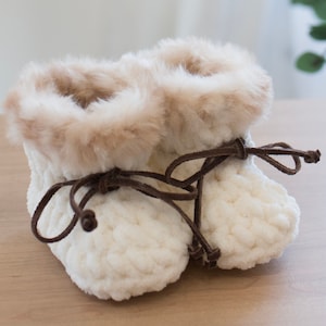 May include: A pair of white crocheted baby booties with brown faux fur trim and brown laces.