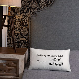 May include: A rectangular white throw pillow featuring the black printed text Radius of nth Bohr's Orbit followed by the physics equation En = - mZ^2e^4 / 8ε0^2h^2n^2. The pillow has a smooth fabric surface and is positioned on a grey quilted bedspread.