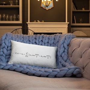 May include: A rectangular white throw pillow featuring the black printed mathematical Fourier series formula f(x) = a0 + sum(n=1 to infinity) (an cos(n*pi*x/L) + bn sin(n*pi*x/L)). The pillow is resting on a light blue chunky knit blanket.