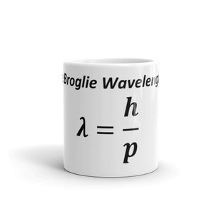 May include: A white ceramic mug featuring the black printed text 'de Broglie Wavelength' and the physics equation lambda equals h divided by p. The mug has a cylindrical shape with a smooth surface and a clear, legible scientific formula displayed.