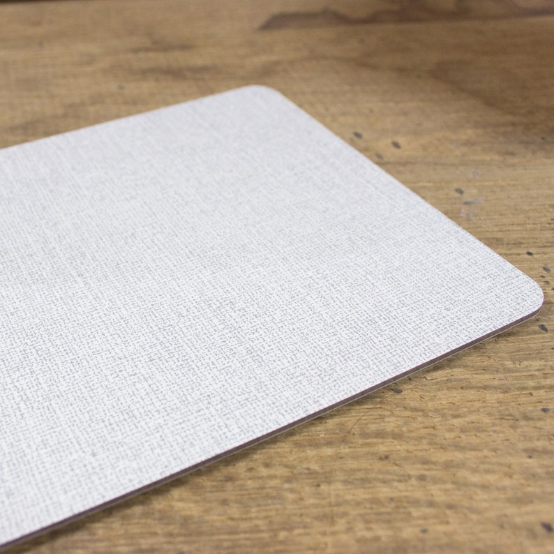 May include: A white placemat with a subtle textured surface. The placemat has a slightly rounded edge.