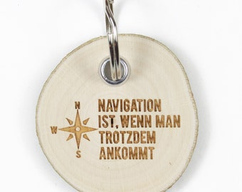 Pode incluir: Um chaveiro redondo de madeira com um design de bússola e o texto "NAVIGATION IST. WENN MAN TROTZDEM ANKOMMT".