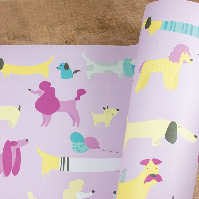 May include: Purple wrapping paper with a repeating pattern of yellow, white, and pink dogs. The dogs are in various poses, including sitting, standing, and running. There are also some balloons in the pattern.