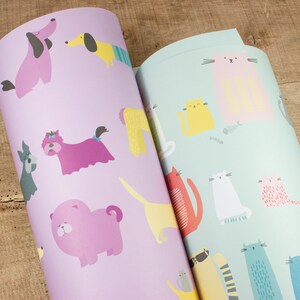 May include: Two rolls of wrapping paper with a repeating pattern of dogs and cats. The dog wrapping paper is purple with pink, yellow, and blue dogs. The cat wrapping paper is light blue with pink, yellow, white, and blue cats.