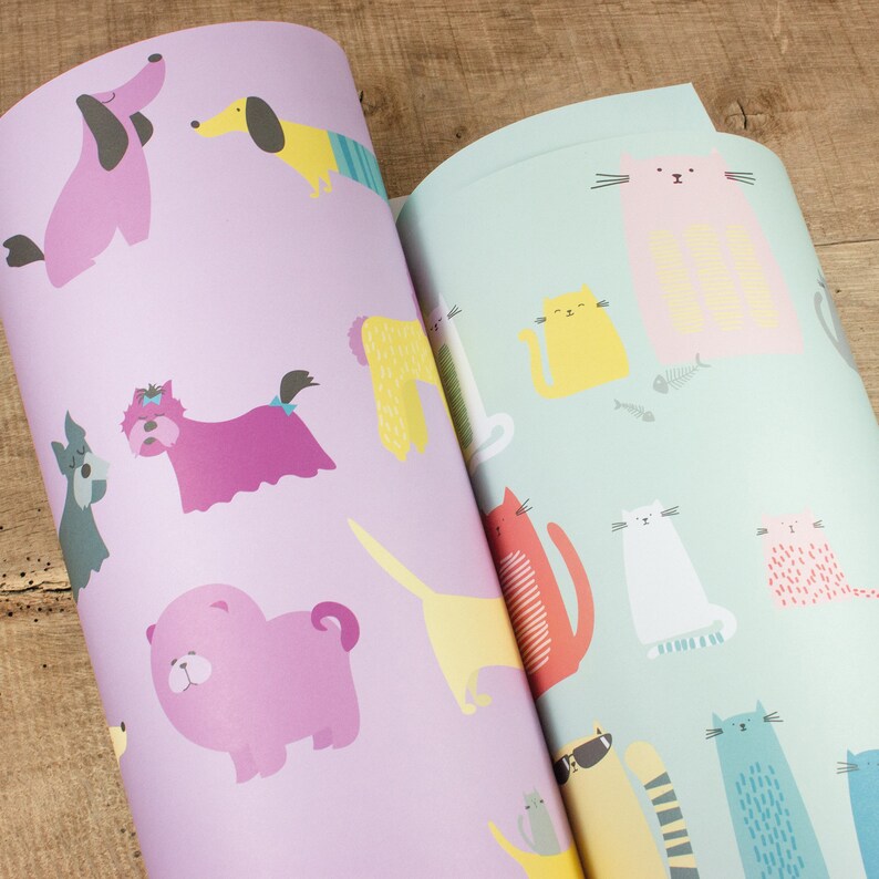 May include: Two rolls of wrapping paper with a repeating pattern of dogs and cats. The dog wrapping paper is purple with pink, yellow, and blue dogs. The cat wrapping paper is light blue with pink, yellow, white, and blue cats.