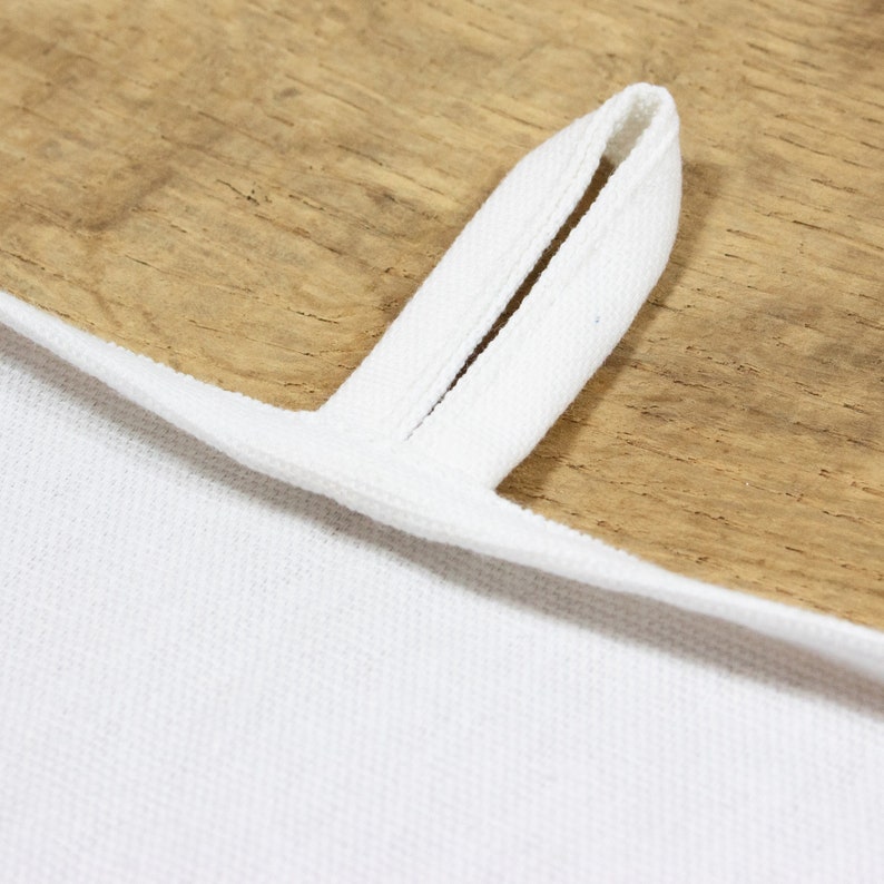 May include: A white cotton tea towel with a loop sewn into the top edge. The loop is made of the same fabric as the towel and is designed to hang the towel on a hook.