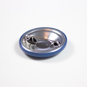Pode incluir: A parte de tr&aacute;s de um bot&atilde;o azul com um pino prateado e uma parte de tr&aacute;s de metal.
