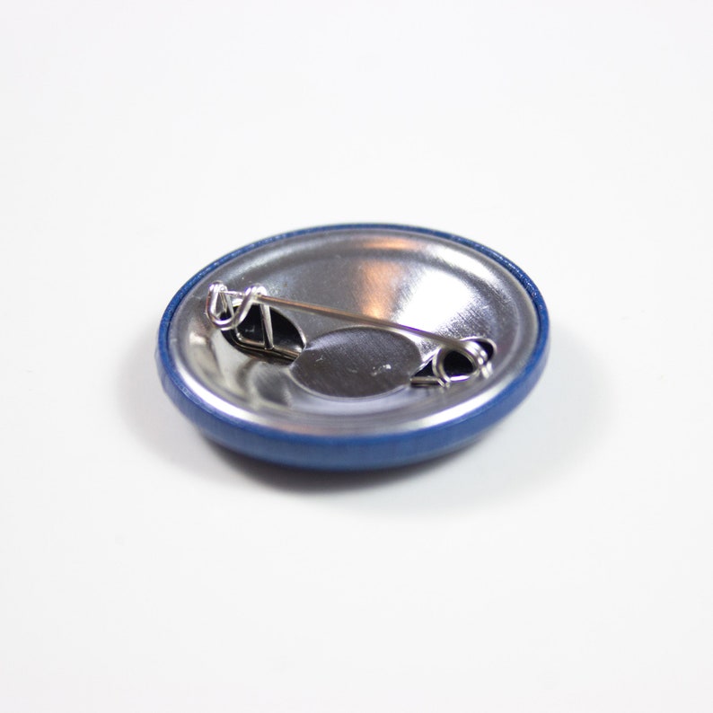 Pode incluir: A parte de tr&aacute;s de um bot&atilde;o azul com um pino prateado e uma parte de tr&aacute;s de metal.