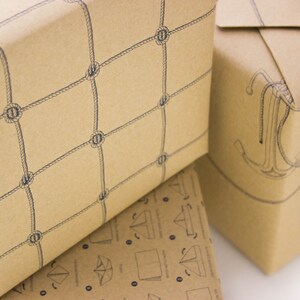 Puede incluir: Dos rollos de papel de regalo marr&oacute;n con dise&ntilde;os n&aacute;uticos. Un rollo presenta un patr&oacute;n de red de cuerda, el otro tiene un dise&ntilde;o de ancla.