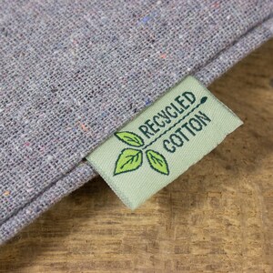 May include: A green fabric label with the text "RECYCLED COTTON" and a green leaf design. The label is attached to a gray fabric.