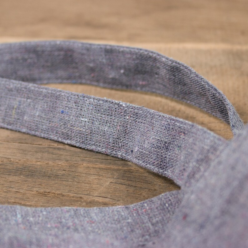 May include: Close-up of a gray linen tote bag with a woven texture. The bag is folded in half, showing the inside of the bag.