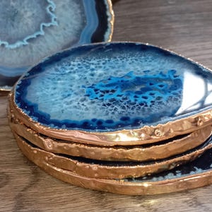 Peut inclure: Ensemble de quatre sous-verres en agate bleue avec une bordure dorée. Les sous-verres sont empilés les uns sur les autres.