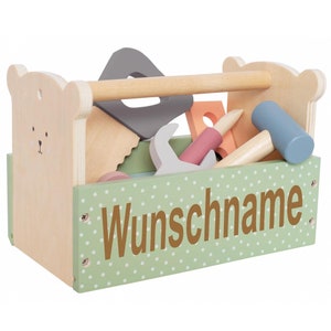 Könnte beinhalten: Eine hölzerne Spielzeug-Werkzeugkiste mit grünem Punkte-Design und einem Bärenkopf an der Seite. Die Werkzeugkiste ist gefüllt mit verschiedenen Holzwerkzeugen, darunter ein Hammer, eine Säge, ein Schraubenschlüssel und ein Schraubendreher. Die Werkzeugkiste hat eine personalisierte Aufschrift, die "Wunschname" lautet.