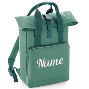 Könnte beinhalten: Ein grüner Canvas-Rucksack mit Rollverschluss und einer Fronttasche. Der Rucksack hat einen weißen gestickten Namen auf der Fronttasche, der "Name" lautet.