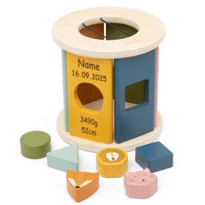 Könnte beinhalten: Ein Holz-Formensortierspielzeug mit einem hellen Holzrahmen und farbigen Paneelen. Die Paneele sind gelb, blau und rosa. Das Spielzeug enthält verschiedene Holzformen, darunter ein Kreis, ein Dreieck, ein Quadrat, ein Fuchs, ein Löwe und eine Katze. Auf der gelben Tafel steht der Text "Name 16.09.2025 3490g 52cm".