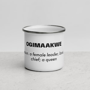 May include: White enamel mug with black text that reads "OGIMAAAKWE noun. a female leader, boss, chief; a queen"