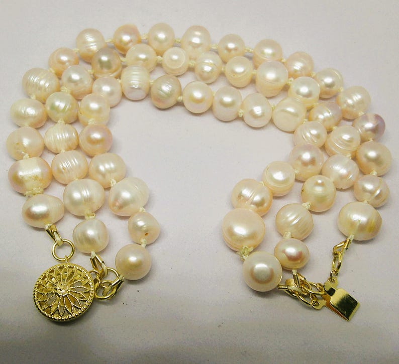 Peut inclure: Un collier de perles multi-rangs avec un fermoir en or. Les perles sont de couleur blanche et cr&egrave;me et ont un l&eacute;ger reflet iris&eacute;.