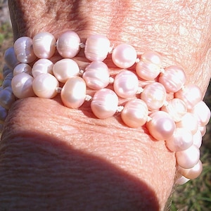 Peut inclure: Un bracelet compos&eacute; de plusieurs rangs de perles roses. Les perles sont rondes et lisses, et elles sont enfil&eacute;es sur un cordon blanc.