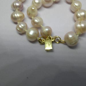 Peut inclure: Un collier de perles avec un fermoir en or. Les perles sont de couleur blanc cr&egrave;me doux et sont enfil&eacute;es sur un fil blanc.