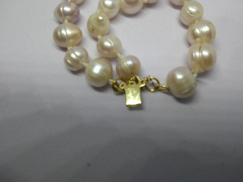 Peut inclure: Un collier de perles avec un fermoir en or. Les perles sont de couleur blanc cr&egrave;me doux et sont enfil&eacute;es sur un fil blanc.