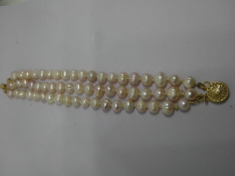 Peut inclure: Un collier de perles &agrave; trois rangs avec un fermoir en or. Les perles sont blanches et ont une l&eacute;g&egrave;re teinte rose.