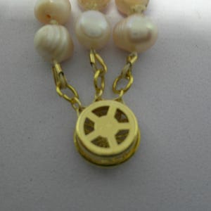 Peut inclure: Un fermoir dor&eacute; avec un motif en forme d'&eacute;toile, attach&eacute; &agrave; un collier de perles.