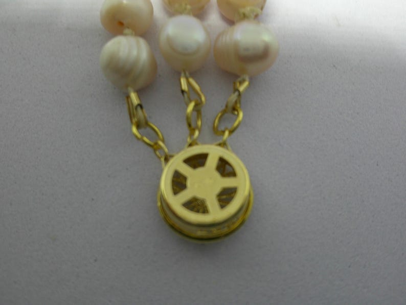 Peut inclure: Un fermoir dor&eacute; avec un motif en forme d'&eacute;toile, attach&eacute; &agrave; un collier de perles.