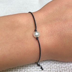 May include: A simple black string bracelet with a single white pearl bead.
