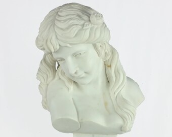 May include: White marble bust sculpture of a woman with long flowing hair and a flower in her hair. The bust is on a white marble pedestal.