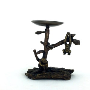 May include: A bronze candle holder shaped like a tree with two monkeys. One monkey is hanging from a branch and the other is sitting on a branch. The candle holder is on a wooden base.