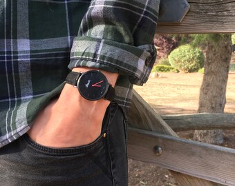 Relógio preto para homem. Básico, minimalista e moderno, com ponteiros vermelhos e pulseira de couro facilmente intercambiável.