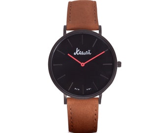 Montre pour garçon avec cadran noir et bracelet en cuir marron. Basique, minimaliste, plat et moderne, avec des aiguilles rouges.