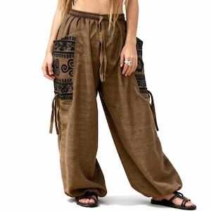 May include: Brown harem pants with black embroidered pocket details and drawstring waist. The loose-fitting pants have a relaxed style and are worn with black sandals. The pockets feature a decorative pattern.