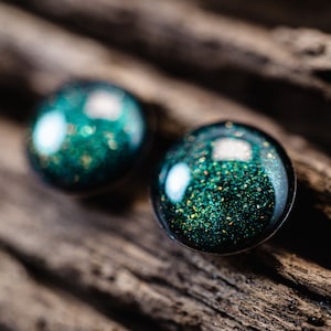 May include: A pair of round, dark green resin earrings with gold glitter embedded in the resin.