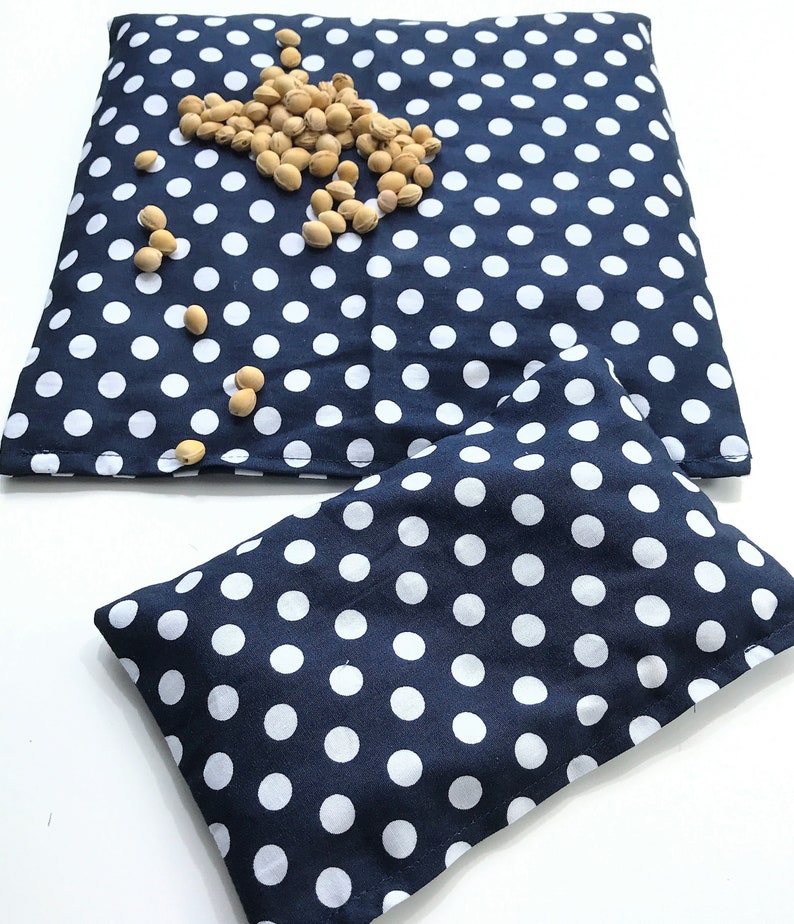 May include: Two blue fabric pouches with white polka dots. The larger pouch is lying flat and the smaller pouch is folded in half. Both pouches are filled with small, beige beans.